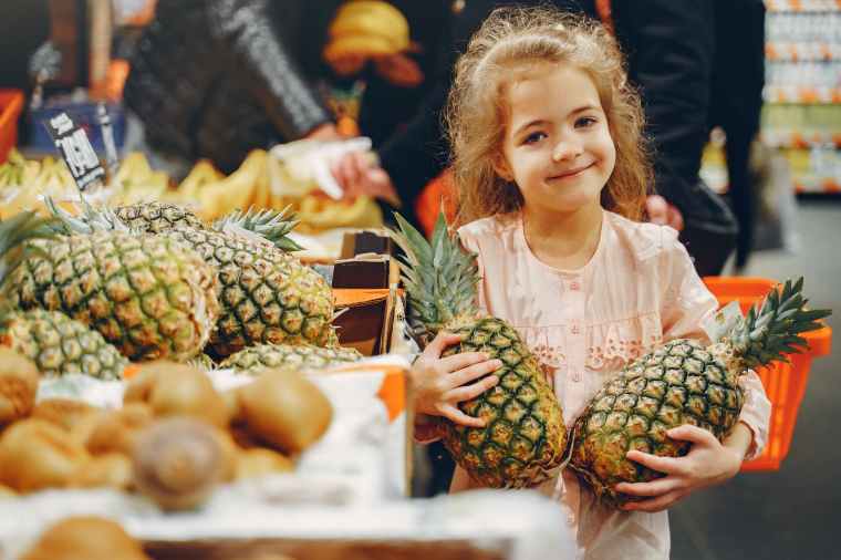 little girl holding two fresh pineapples